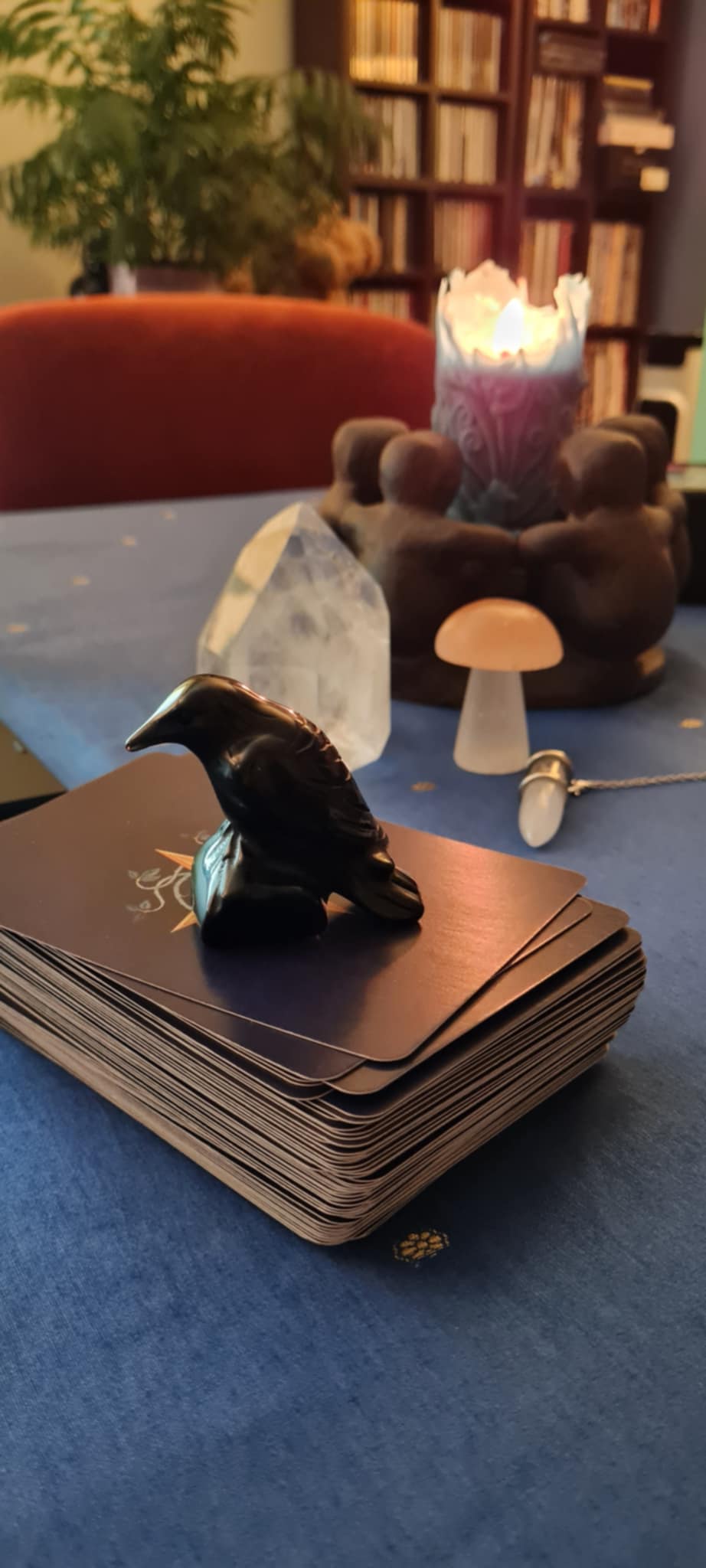 Stack of oracle cards with a small figurine on top, in front of a candle and healing crystal items on a table.