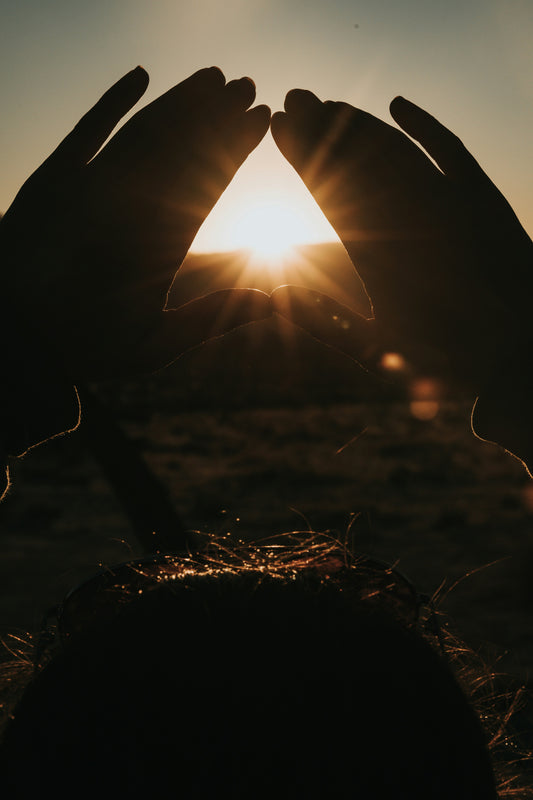 Silhouette of hands framing a bright light source against a dark background